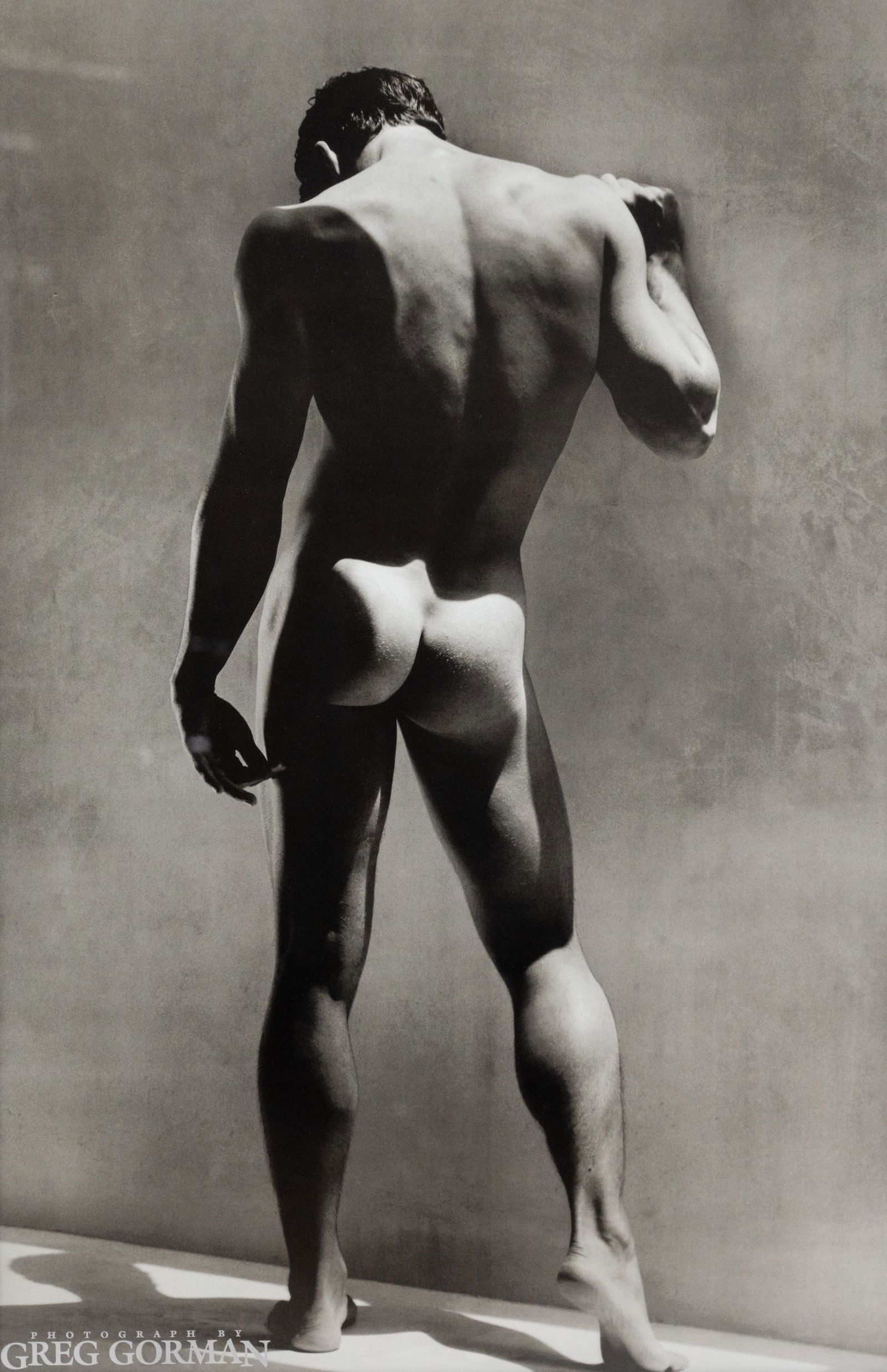 Greg Gorman Male Nude Photograph Print: A Greg Gorman (American, 1949-) black and white photograph print poster depicting a standing nude male figure printed "Photograph by Greg Gorman at lower left corner. Housed in wood frame with matting