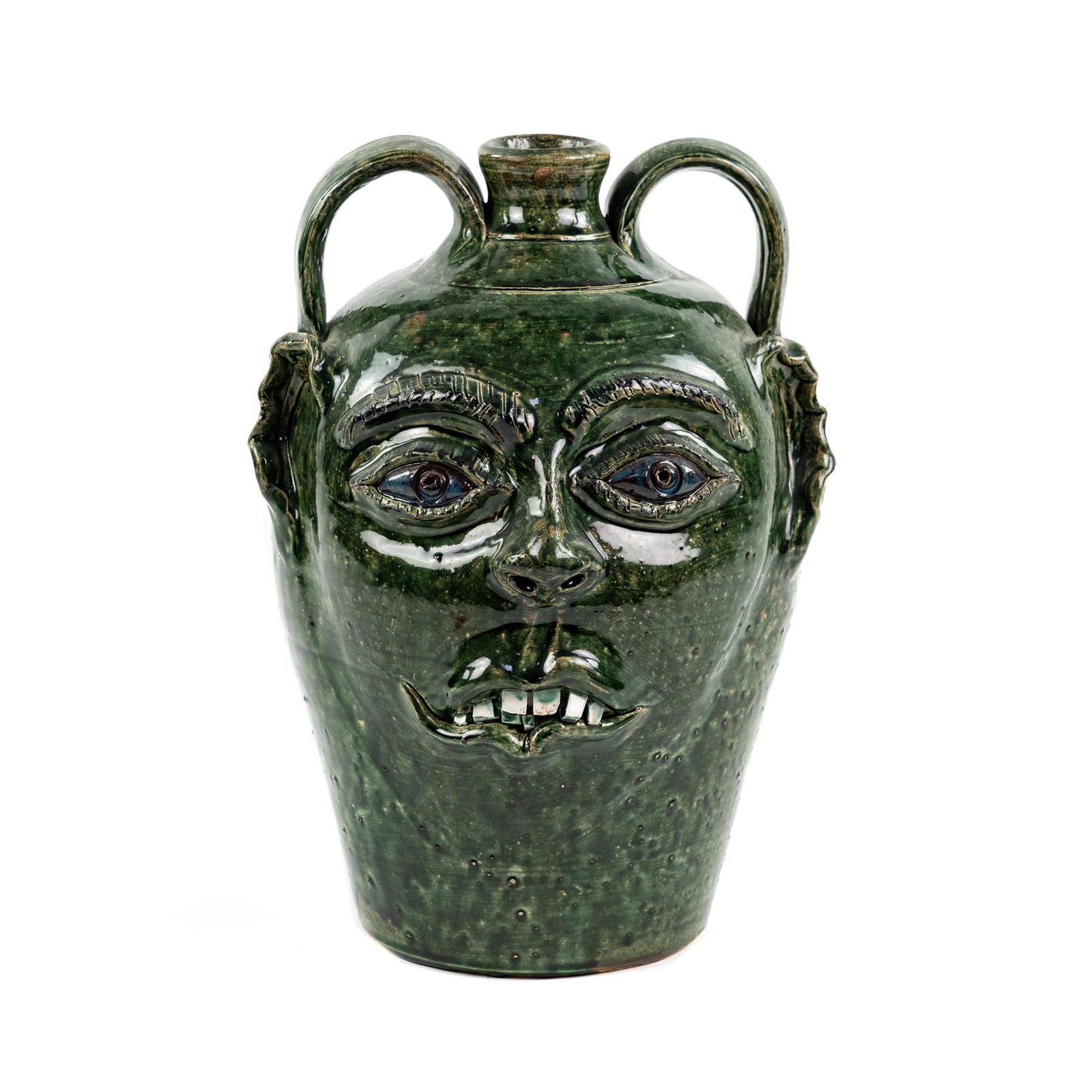 Bobby Ferguson Green Face w/ Ears Ceramic Jug: A Bobby Ferguson (American, b. 1933) southern Folk Art green glazed ceramic jug with two handles depicting a face with protruding eyes, crooked teeth, and folded ears. Incise signed on side near botto