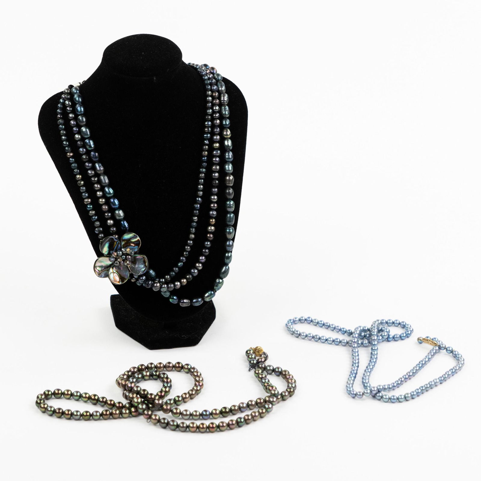(3) Cultured and Natural Pearl Necklaces w/ Brooch: A group of three (3) pearl necklaces including a multi-strand natural pearl necklace with magnetic clasp having purple and blue colored pearls and an abalone flower brooch, and two cultured pearl neck