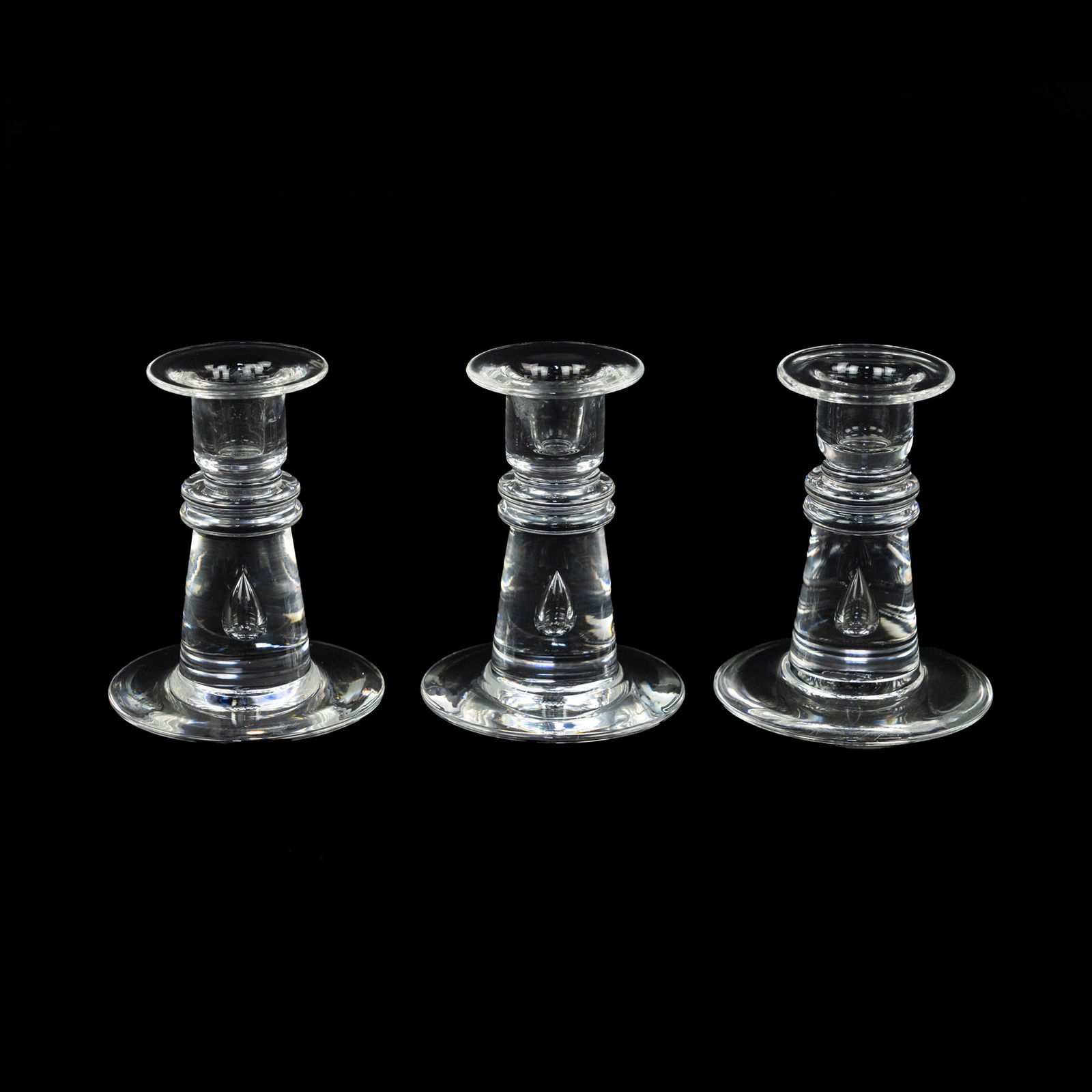 (3) Steuben Crystal Teardrop Candlestick Holders: A group of (3) Steuben crystal candle holders having tapered stems, flared bases, and featuring a revolve design in the center of the stem and a teardrop motif near the base. Incised marked on undersi