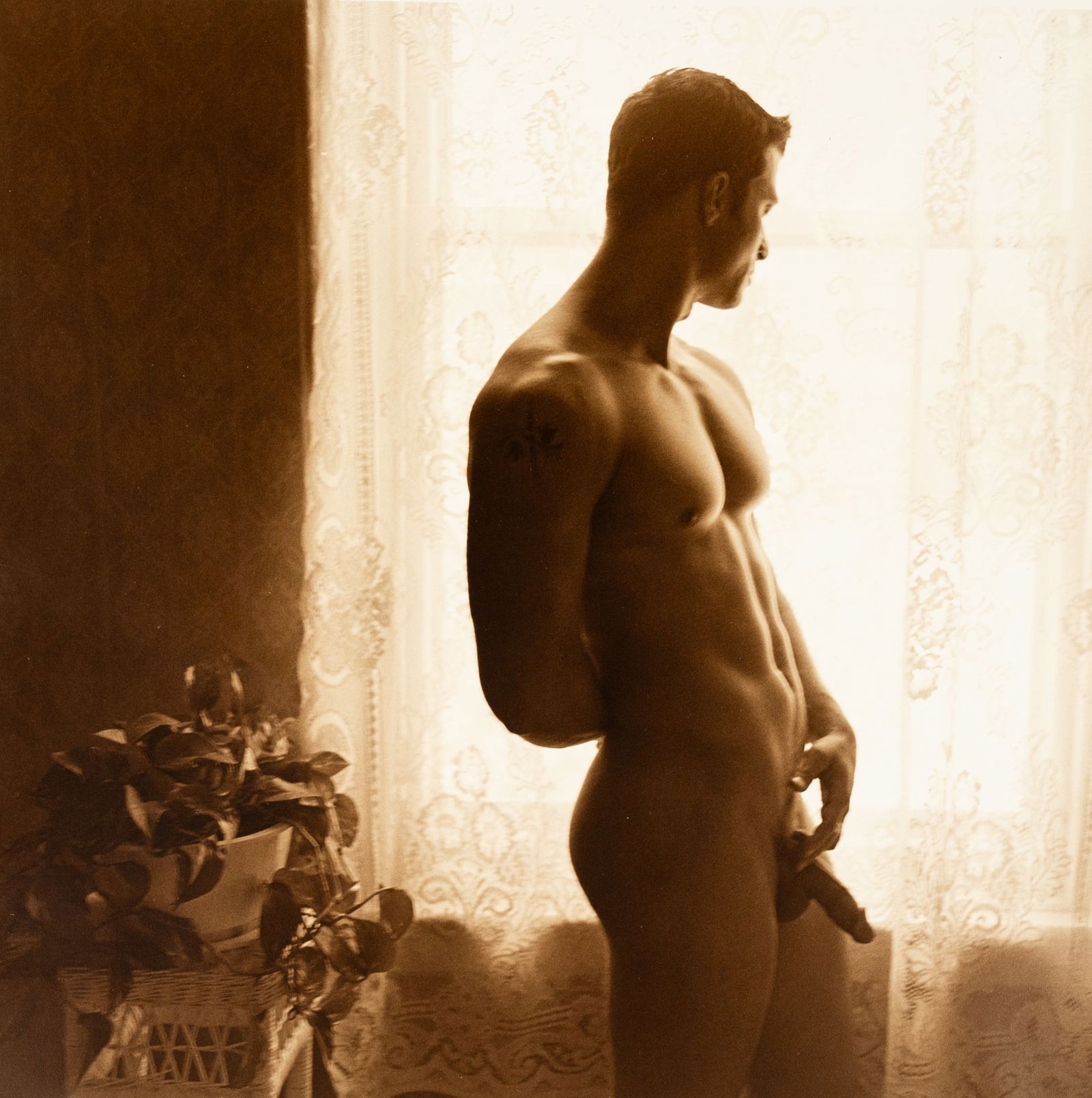 James Spada 'Tom' Male Nude Sepia Tone Photograph: A James Spada (American, b.1950) sepia tone photograph titled 'Tom' depicting a nude man standing near a window. Signed and dated '99' in lower right and editioned 1/1 lower left. Titled and stickered