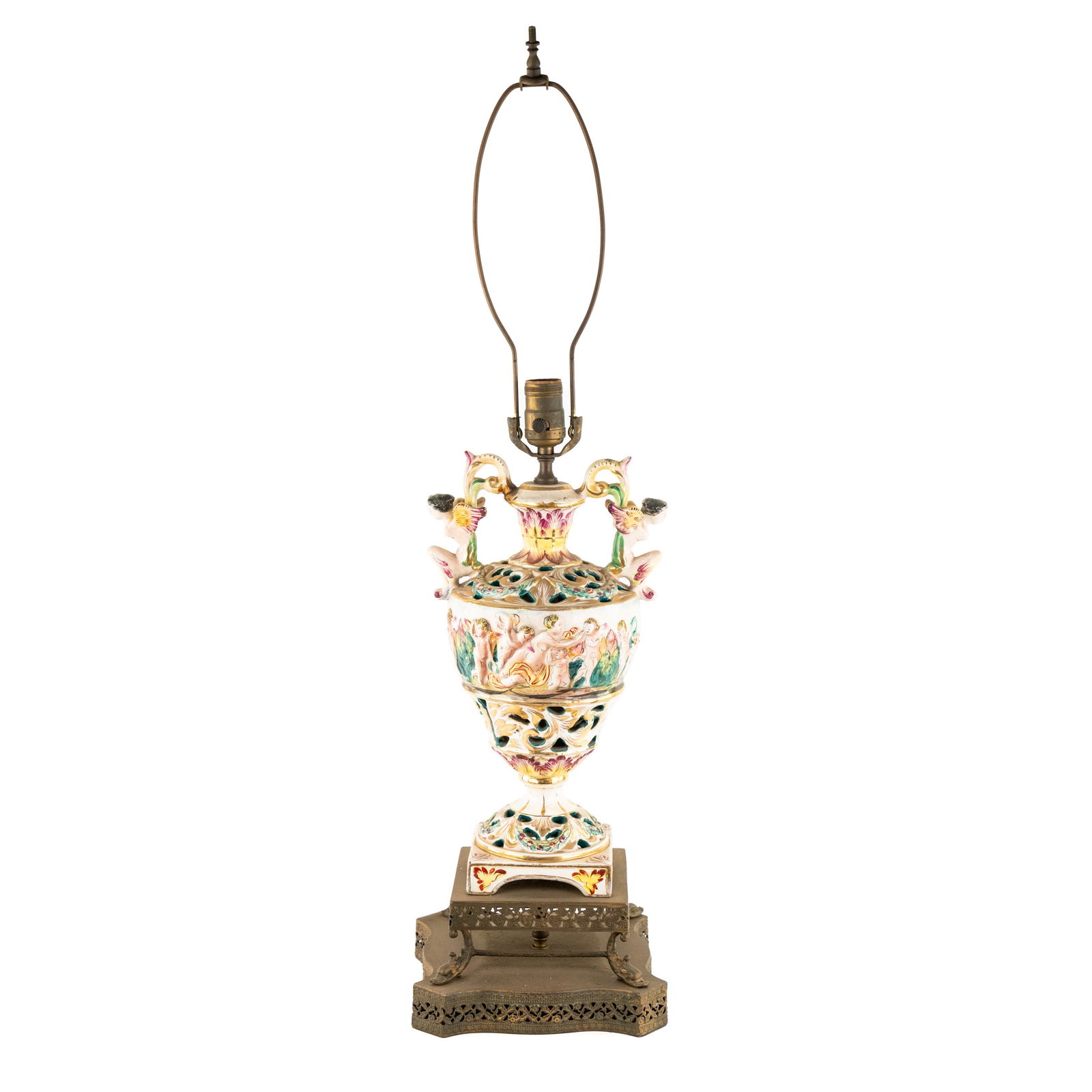 Italian Capodimonte Porcelain Table Lamp: An Italian capodimonte porcelain table lamp having a floral motif pierced brass base and a porcelain body with loop handles in the form of winged women, and featuring a large central hand painted moti