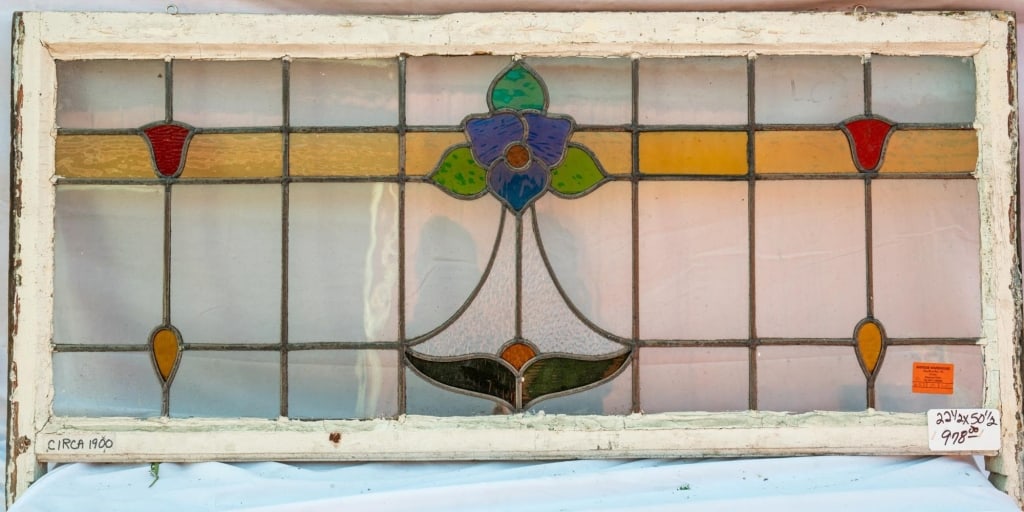 FRENCH ART NOUVEAU STAINED GLASS PANEL: French Art Nouveau stained glass panel with a blue glass flower, accented with amber and red stained glass, set within colorless and amber leaded glass panels. Approximate dimensions: h. 22.5", w. 55.