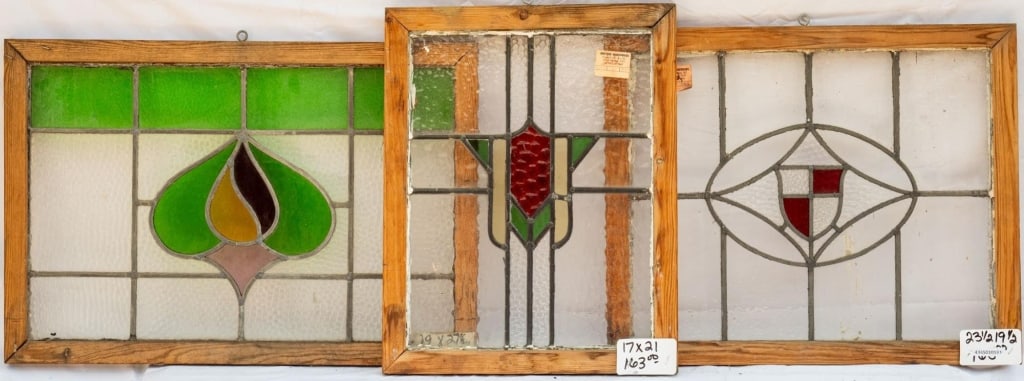 THREE FRENCH STAINED GLASS PANELS: Three French stained glass panels: one with a shield-shaped medallion, one with geometric detail, and one with a floral detail. Approximate dimensions: h. 19", w. 27.5" Disclaimer: This is an online c