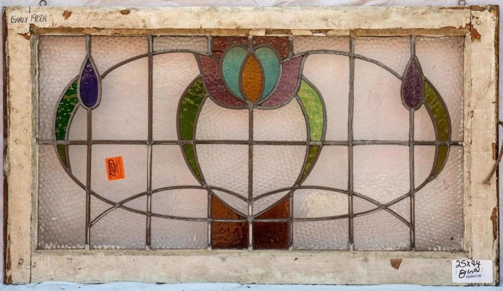 FRENCH ART NOUVEAU STAINED GLASS PANEL: French Art Nouveau stained glass panel with a central floral motif flanked by two symmetrical purple floral accents. Approximate dimensions: h. 25", w. 44" Disclaimer: This is an online court ordered