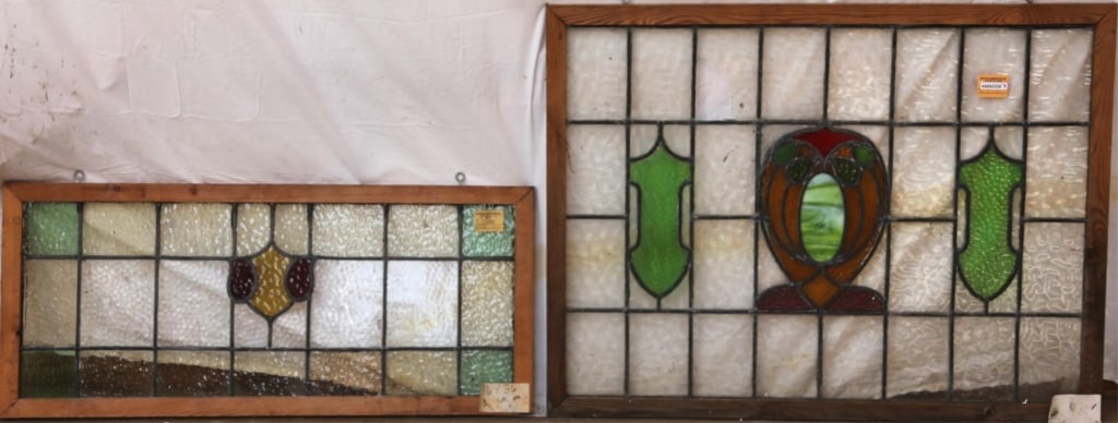 TWO ANTIQUE CONTINENTAL STAINED GLASS PANELS: Two antique Continental stained glass panels, one with a shield-shaped amber and red medallion, the other with an abstract multicolored medallion featuring a green wispy glass accent. Approximate dime