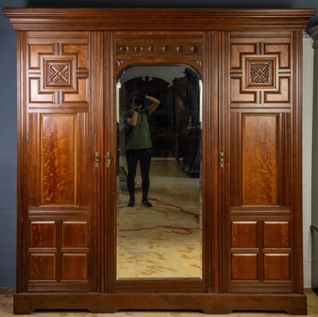 ENGLISH MAHOGANY TRIPLE DOOR ARMOIRE: English mahogany triple-door armoire with plumb pudding mahogany panels, carved rosettes, and beveled mirror. Approximate dimensions: h. 83.25", w. 84", d. 25.25 Disclaimer: This is an online court or