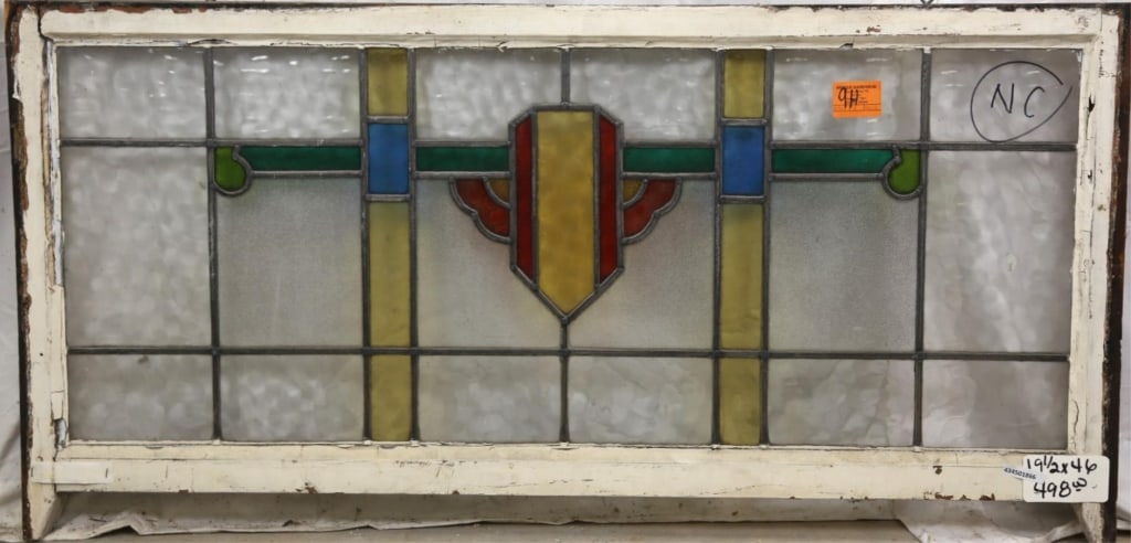 ENGLISH ART DECO STAINED GLASS PANEL: English Art Deco stained glass panel with yellow and red shield-shaped medallion and green and blue accents. Approximate dimensions: h. 19.5", w. 46" Disclaimer: This is an online court ordered bankru