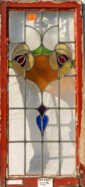 FRENCH ART NOUVEAU STAINED GLASS PANEL: French Art Nouveau stained glass panel with a heart-shaped medallion with a floral motif, textured amber glass panels, and green, purple, and blue accents. Approximate dimensions: h. 44", w. 20" Discl