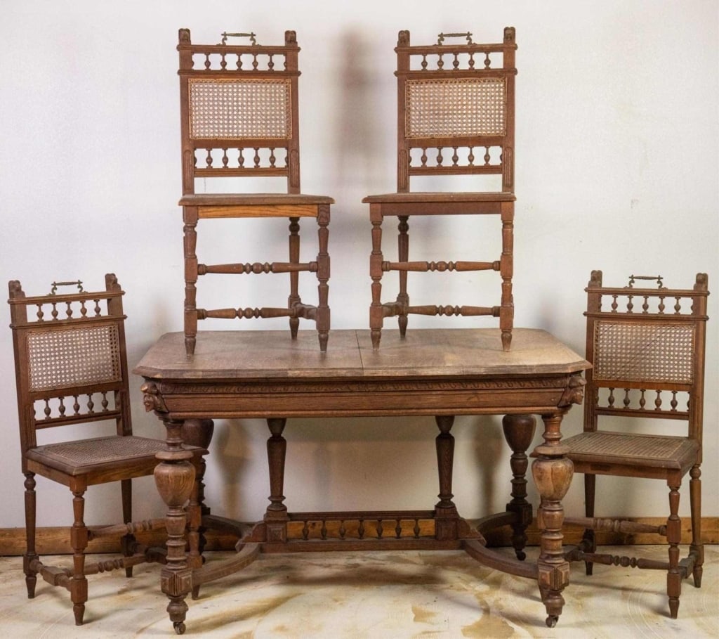 FRENCH OAK WINE TASTING TABLE & 4 CHAIRS: French oak wine tasting table with figural carved details and castered legs, accompanied by four chairs with ornate lift handles and cane back and seats. Approximate dimensions: table: h. 30", w. 51",