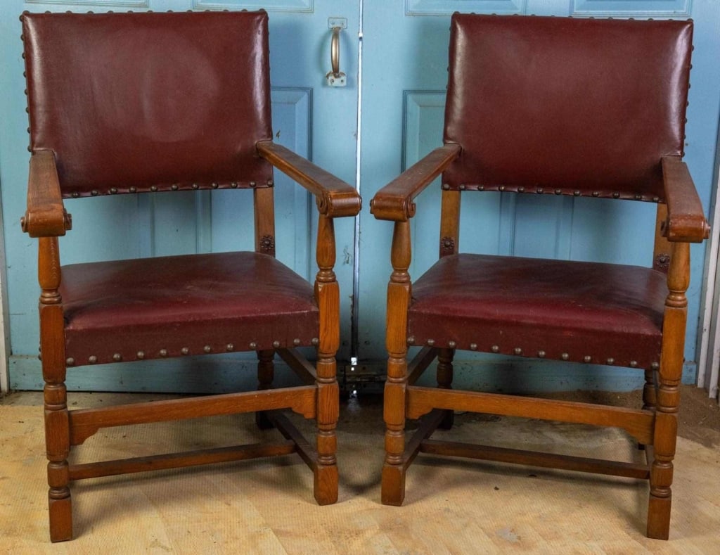 PAIR OF ENGLISH NAILHEAD TRIM LEATHER ARMCHAIRS: Pair of English leather armchairs with oxblood leather seats and backs, nailhead trim accents, and carved details. Approximate dimensions: h. 40.5", w. 26", d. 24" Disclaimer: This is an online court