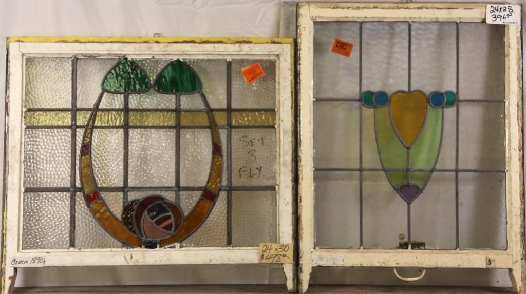 TWO FRENCH ART NOUVEAU STAINED GLASS PANELS: Two French Art Nouveau stained glass panels, one with rose medallion, wispy glass leaves, and amber and red garland detail, the other with shield-form medallion. Approximate dimensions: h. 28", w. 24"