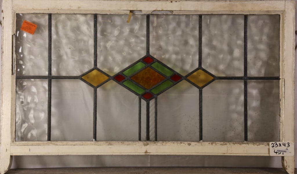 IRISH ART DECO STAINED GLASS PANEL: Irish Art Deco stained glass panel with rhombic amber, green, and red central medallion, and two yellow rhombic accents on the sides. Approximate dimensions: h. 23", w. 43" Disclaimer: This is an onli