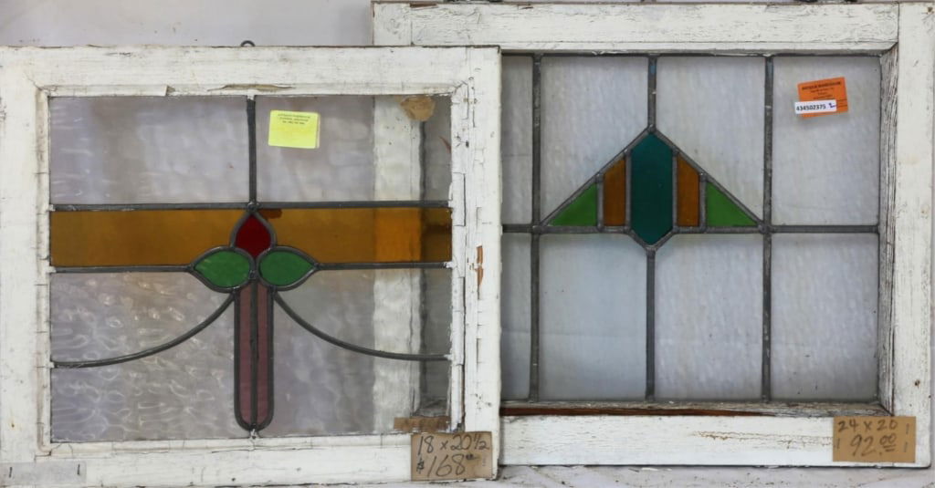 TWO CONTINENTAL STAINED GLASS PANELS: Two Continental stained glass panels, one with a floral motif medallion in pink, amber, red, and green, and the other with a triangular geometric medallion in amber and green. Approximate dimensions: