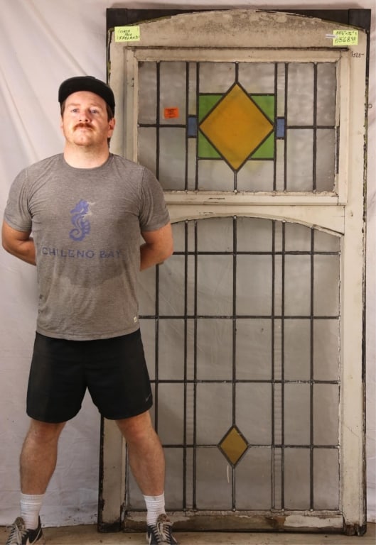 IRISH ART DECO STAINED GLASS PANEL: Irish Art Deco stained glass panel with yellow rhombic medallion with green and blue geometric accents. Approximate dimensions: h. 76", w. 38.5" Disclaimer: This is an online court ordered bankruptcy