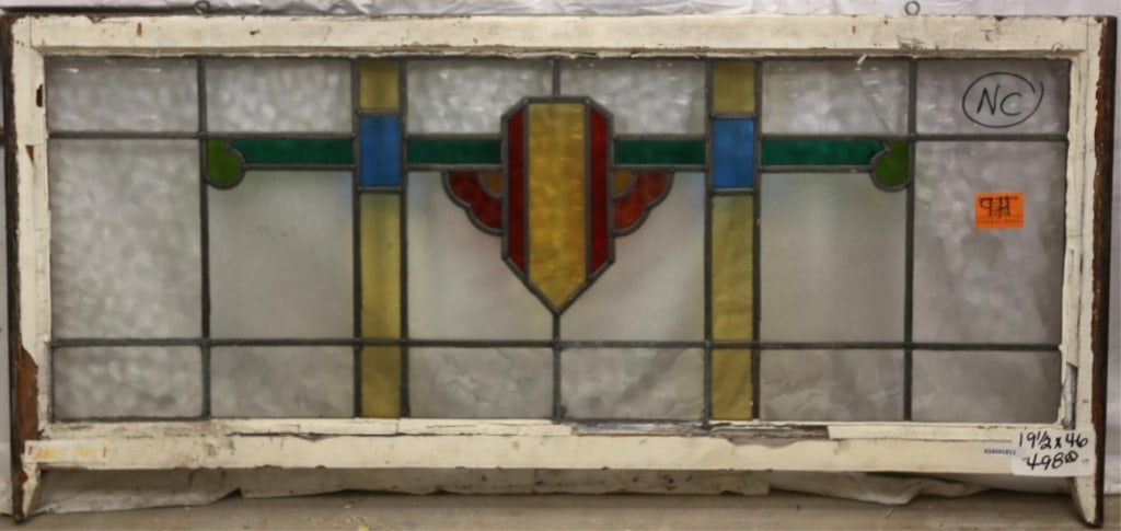 ENGLISH ART DECO STAINED GLASS PANEL: English Art Deco stained glass panel with yellow and red shield-shaped medallion and green and blue accents. Approximate dimensions: h. 19.5", w. 46" Disclaimer: This is an online court ordered bankru