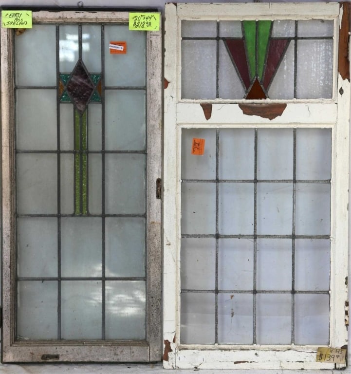 TWO LARGE IRISH STAINED GLASS PANELS: Two large Irish stained glass panels, one with a geometric medallion and purple wispy glass accents, and the other with a geometric medallion in purple, green, and amber. Approximate dimensions: h. 44