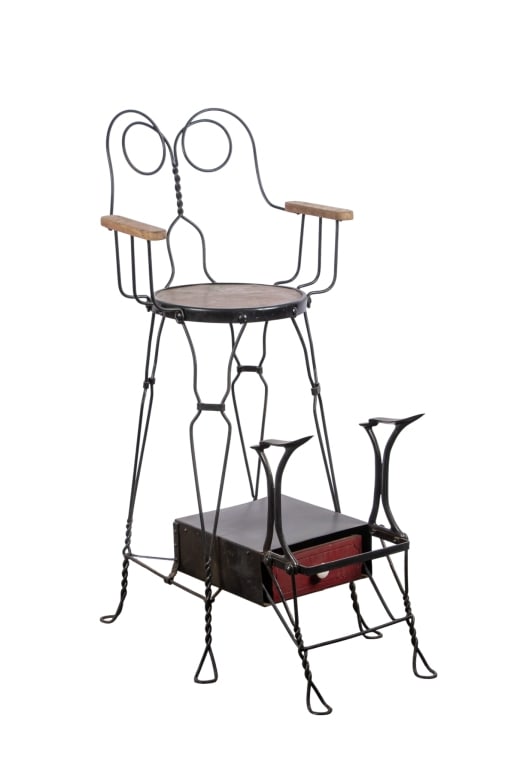 WROUGHT & CAST IRON SHOESHINE CHAIR: American wrought and cast iron shoeshine chair with wrought iron heart-shaped back, wooden armrests, padded brown seat, and extendable cast iron shoe rests on bottom. Approximate dimensions: h. 52.5",