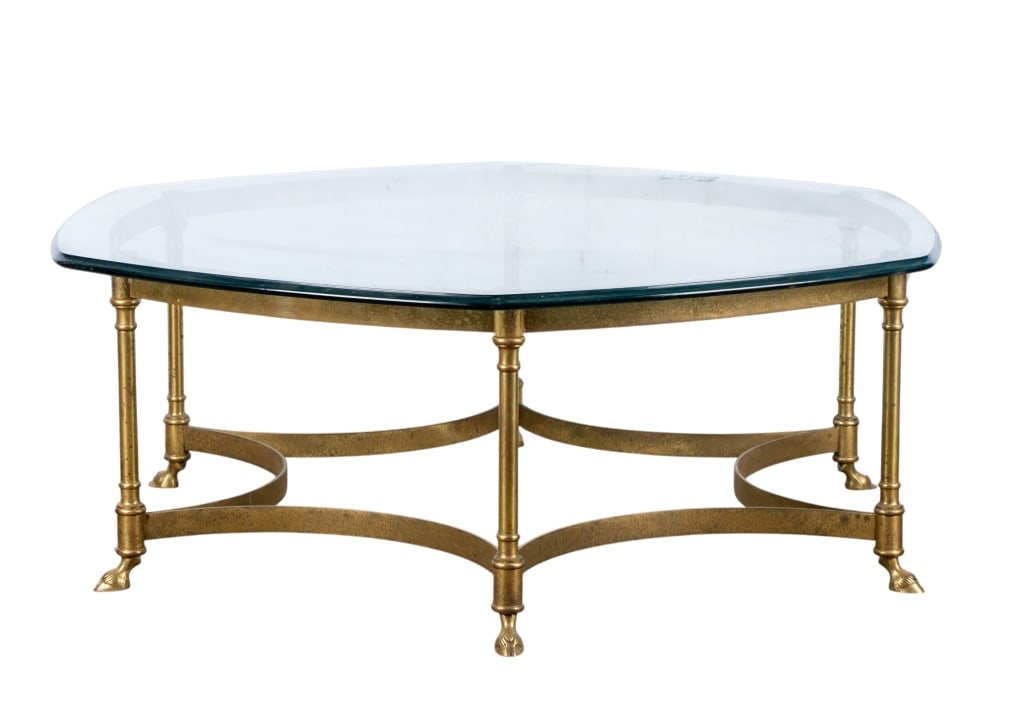 HOLIDAY REGENCY BRASS AND GLASS TOP COCKTAIL TABLE: Holiday Regency brass and glass top cocktail table with hoof feet. Approximate dimensions: h. 15", w. 43", d. 43" Disclaimer: Participating bidders must have a credit card on file with