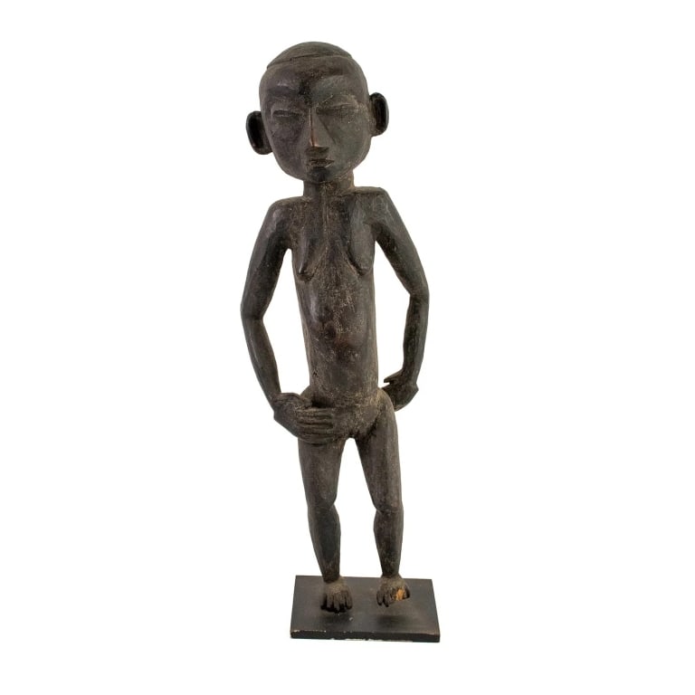 AFRICAN HAND-CARVED EBONY FERTILITY IDOL: African Ivory Coast hand-carved ebony wood female fertility idol depicting a nude pregnant woman with elongated features presented on a square black painted metal stand. Approximate dimensions: h.