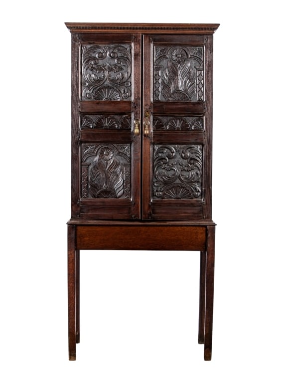 NEO-GOTHIC STYLE OAK CUPBOARD ON STAND: Neo-gothic style oak cupboard on stand with inset carved panels and brass teardrop pulls. Approximate dimensions: h. 65.5", w. 27", d. 15" Disclaimer: Participating bidders must have a credit card on