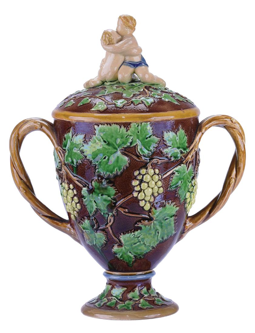 Minton Majolica Loving Cup & Cover, c.1860: (after a design for the Art Union), Brown glaze, decorated with vine leaves and grapes, two entwined branch lug handles, the lid surmounted with two entwined cherubs, all atop a circular cushioned bas