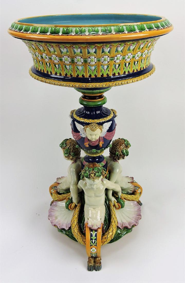 Rare Minton majolica monumental: centerpiece c.1875 modeled as three back to back linked arm cherubs between shells and garlands and supported by three scroll feet, a central vase with angel masks supporting a large circular pierced