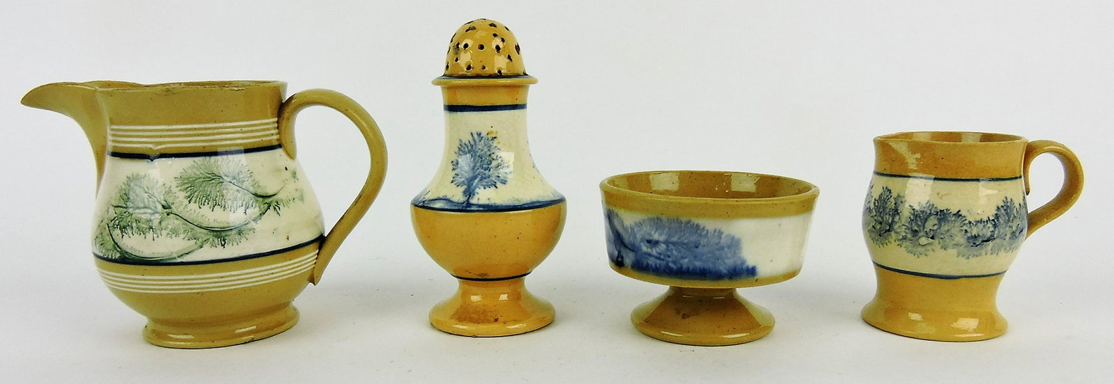 Mochaware yellow lot of 4 pieces;: 3 1/2" creamer with green seaweed, castor/shaker with blue seaweed, nick to top, 4 1/2", footed salt cellar with blue seaweed, and 2 1/2" creamer with blue seaweed