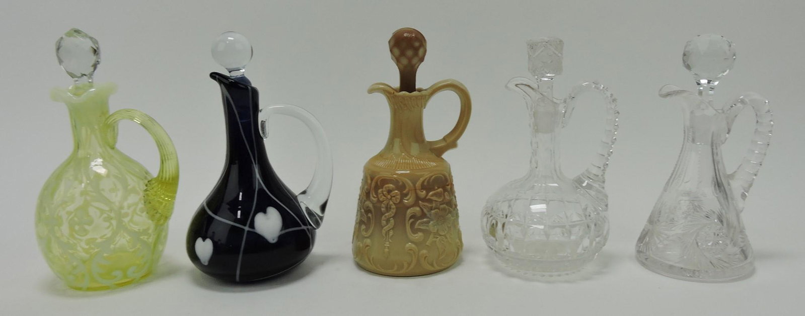 Lot of 5 cruets: vaseline Spanish Lace: (hairline), Gibson hanging hearts, McKee chocolate wild rose with bowknot (hairline to spout), and 2 cut glass