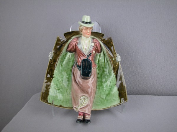 Majolica figural match holder of lady with open t: Majolica figural match holder of lady with open trench coat minor repair to tip of coat, 8 1/2"