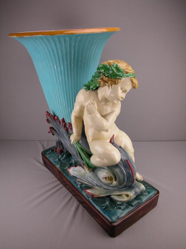 MINTON monumental majolica floor jardiniere in t: MINTON monumental majolica floor jardiniere in the form of a cherub riding a dolphin terminating in a turquoise trumpet shaped flower vase, designed by Hughes Protat, shape no. 808, professional repai