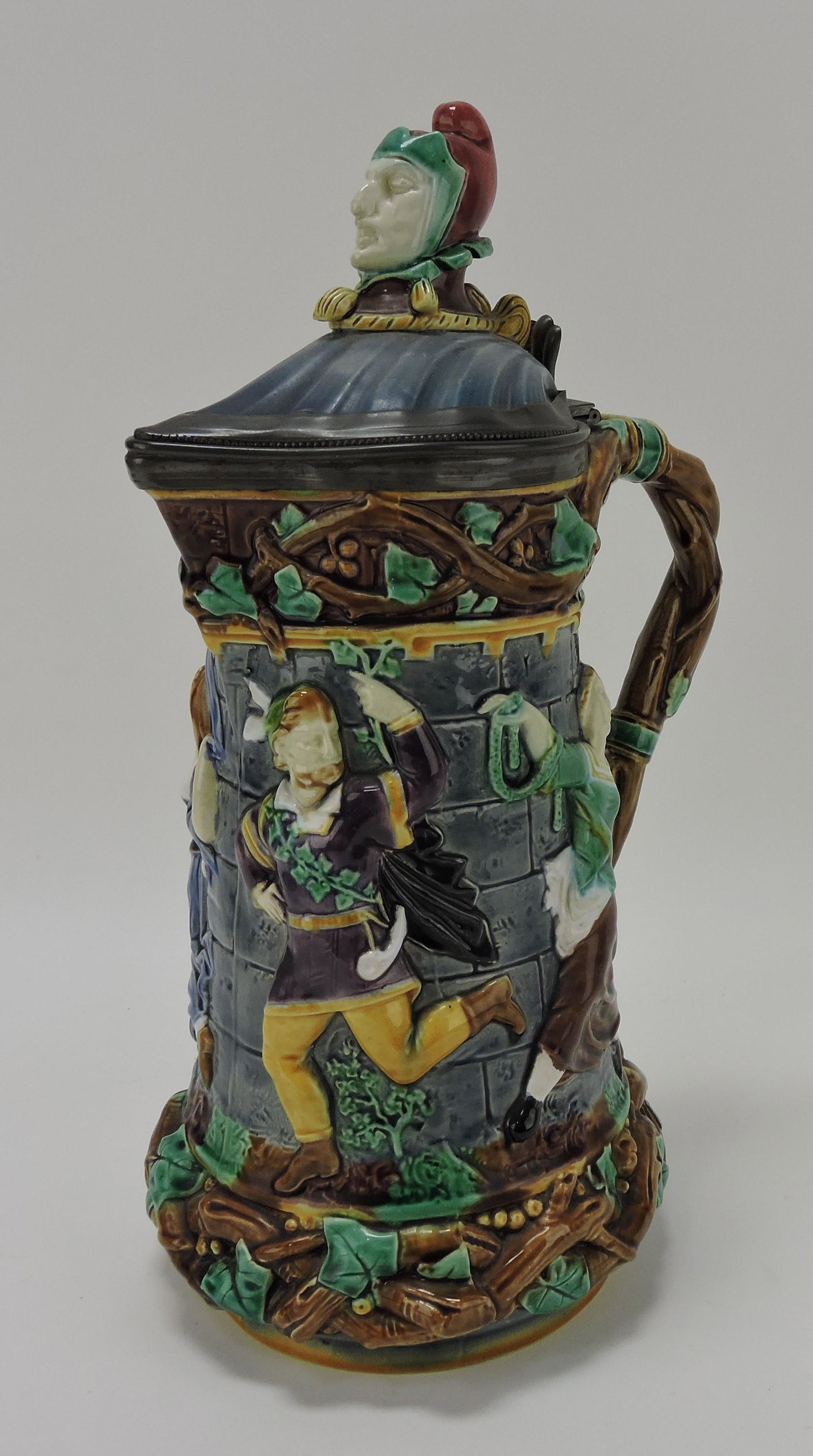 Minton majolica 'Tower' jug with jester: finial, figures of people dancing in the street in high relief, 13", shape no. 1231, professional rim repair to lid; REF: Majolica Mania by Weber, Vol 1, p. 48