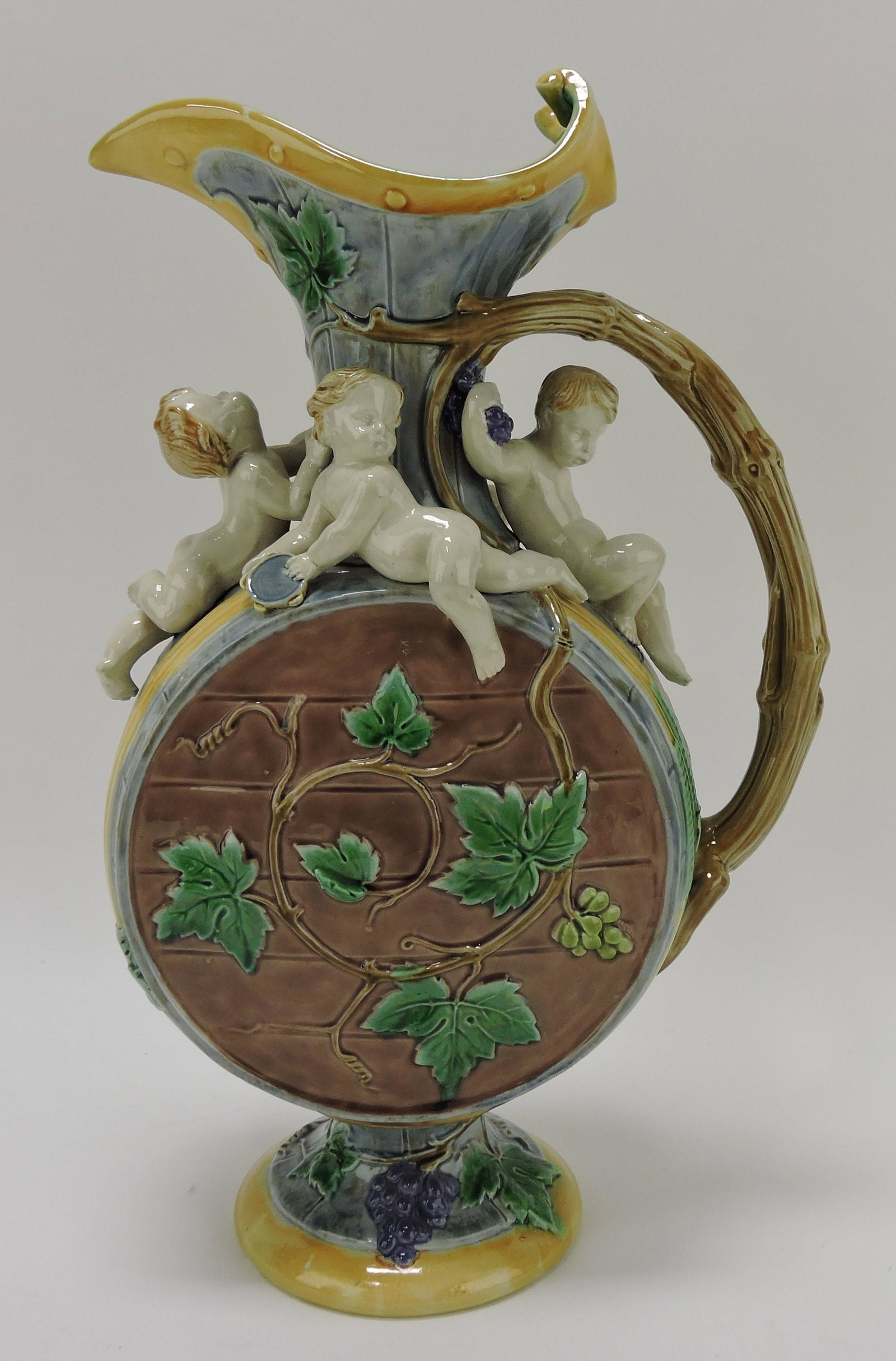 Minton majolica 'Protat' ewer designed by: Hughes Protat with circular body as a barrel with grapevine handle and applied putti, monogram for Hughes Protat under handle, 15", shape no. 900; REF: Majolica Mania by Weber, Vol 2, p. 71