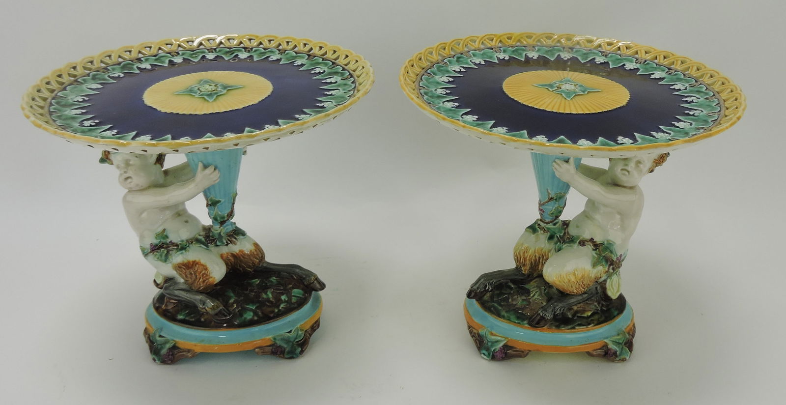 Wedgwood majolica pair of comports,: each with a fawn supporting a cobalt plate with grapes and grapevine with wicker rim, one plate professionally reattached, one with professional rim repair, 8"h, 9"d