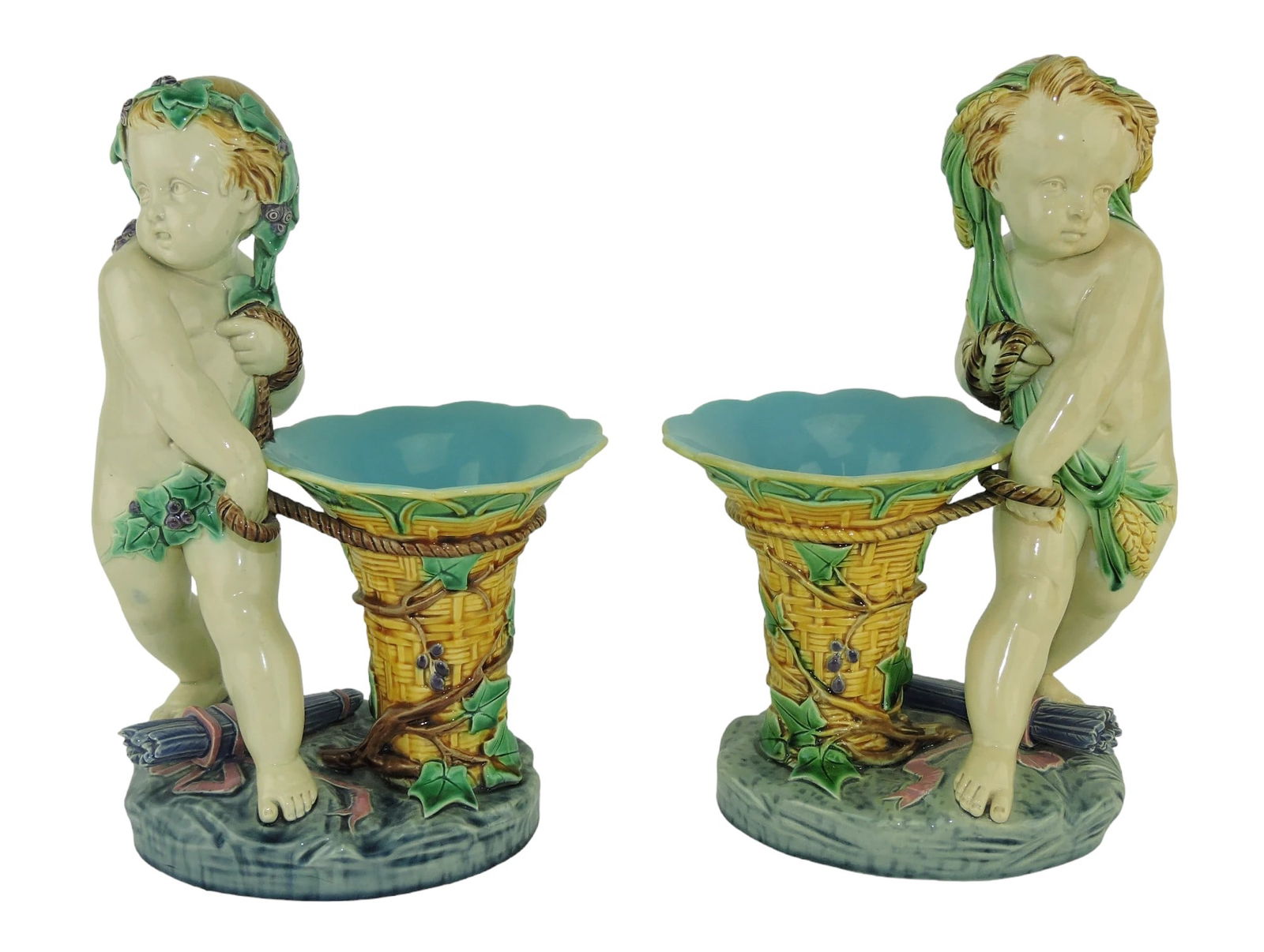 Pair of Minton Majolica Vintager with: basket Posy Vases c.1865, designed by Carrier Bellouse, each modelled as a putto stood over a quiver, one with draped vine, the other with draped wheat, both stood aside a flared basket, all upon a gr
