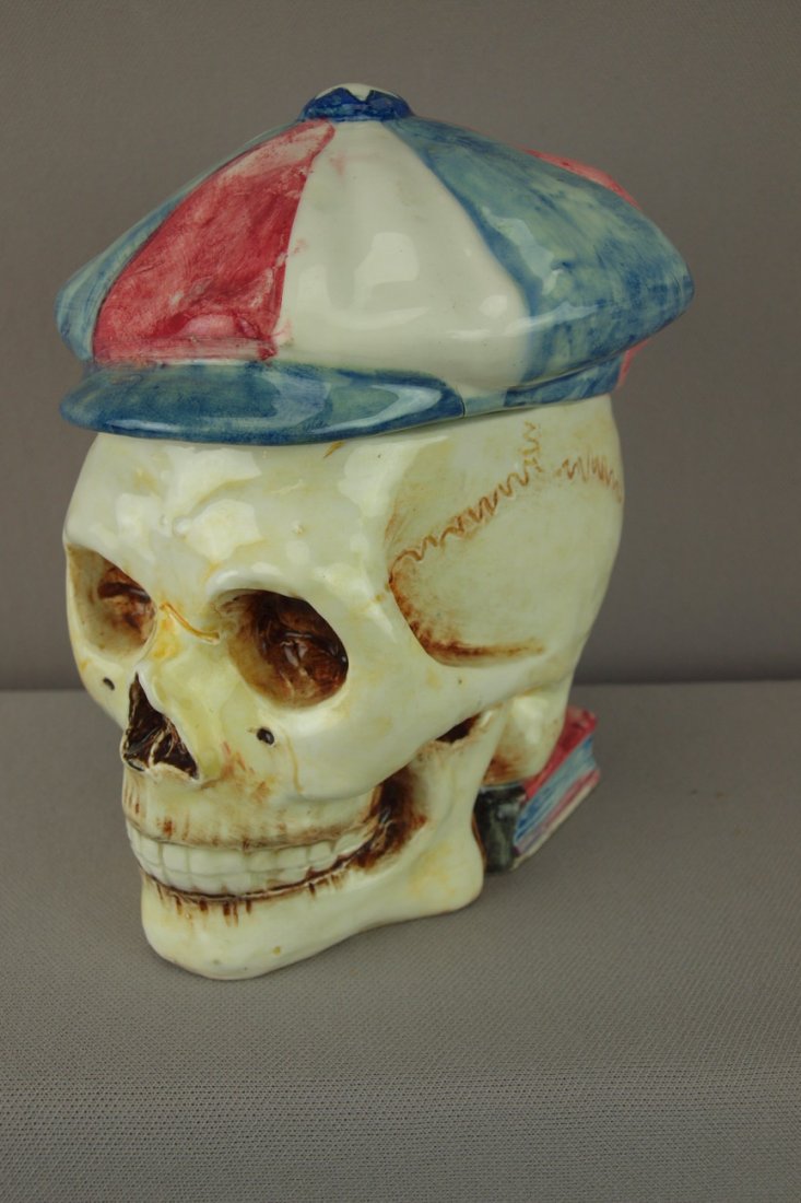Continental majolica figural tobacco jar in the f: Continental majolica figural tobacco jar in the form of a skull with red, white and blue hat resting on book, 7"
