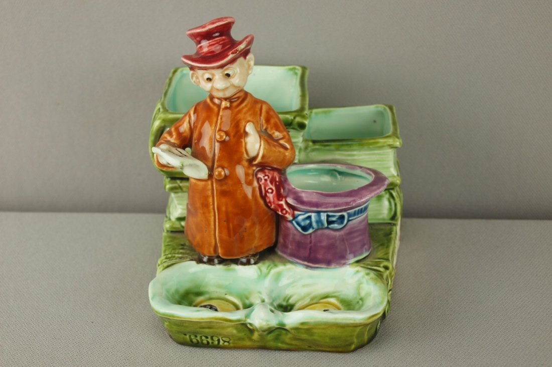 Continental majolica figural match striker of hob: Continental majolica figural match striker of hobo with stack of books, rim nick to hat, 5"