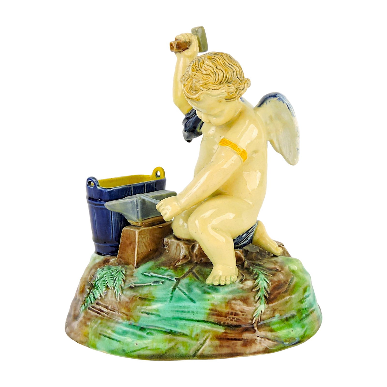 Joseph Holdcroft Majolica Match: Holder c.1875, modelled as cupid with hammer in hand, forging arrows on an anvil, an oval barrel besides, all upon a grassy ground base. 7", professional repair to anvil point. Catalogued and curated 