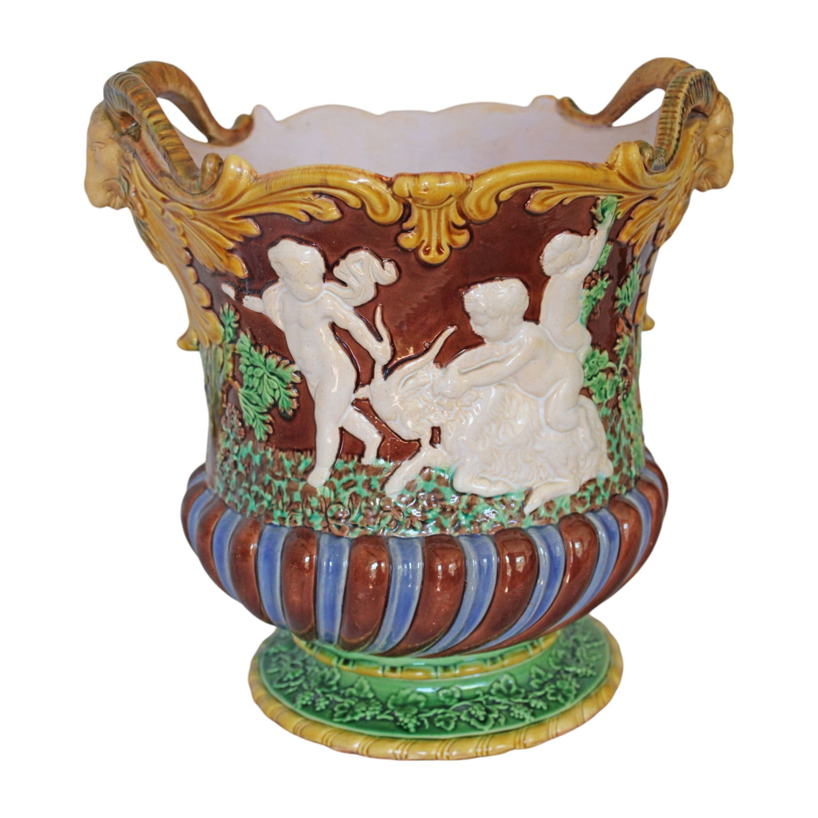 Minton majolica wine cooler of: Bacchanalian figures in relief on each side and goat head handles on a brown ground, 10"h, 9 1/2"w date code for 1859 and Minton marks to base
