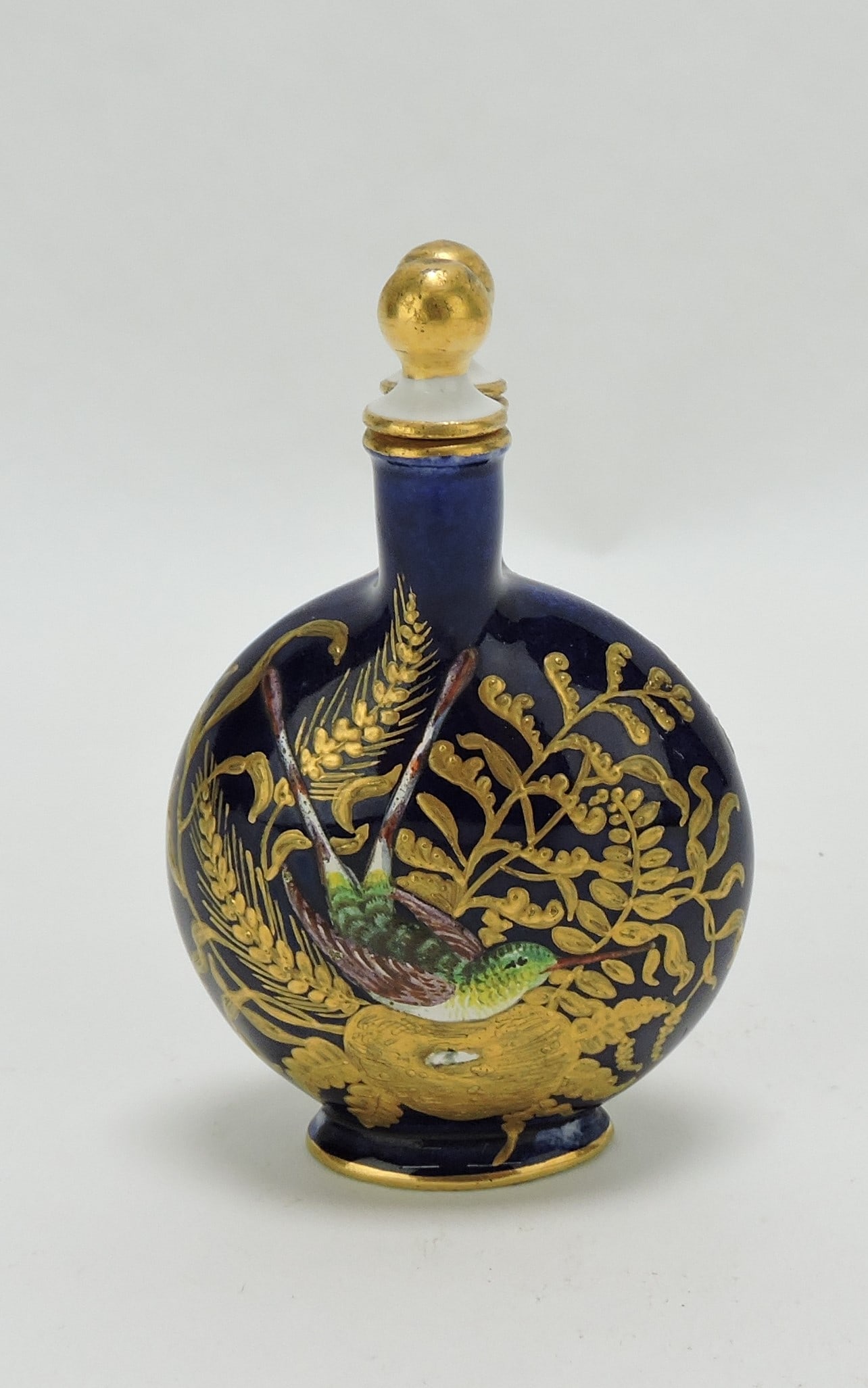 Coalport Porcelain Aesthetic Movement: Scent Bottle and Stopper c.1890, the cobalt body decorated with a brightly enamelled hummingbird among 22ct gilt fauna, with a spherical 22ct gilt stopper. 3 1/2". Catalogued and curated by Nicolaus B