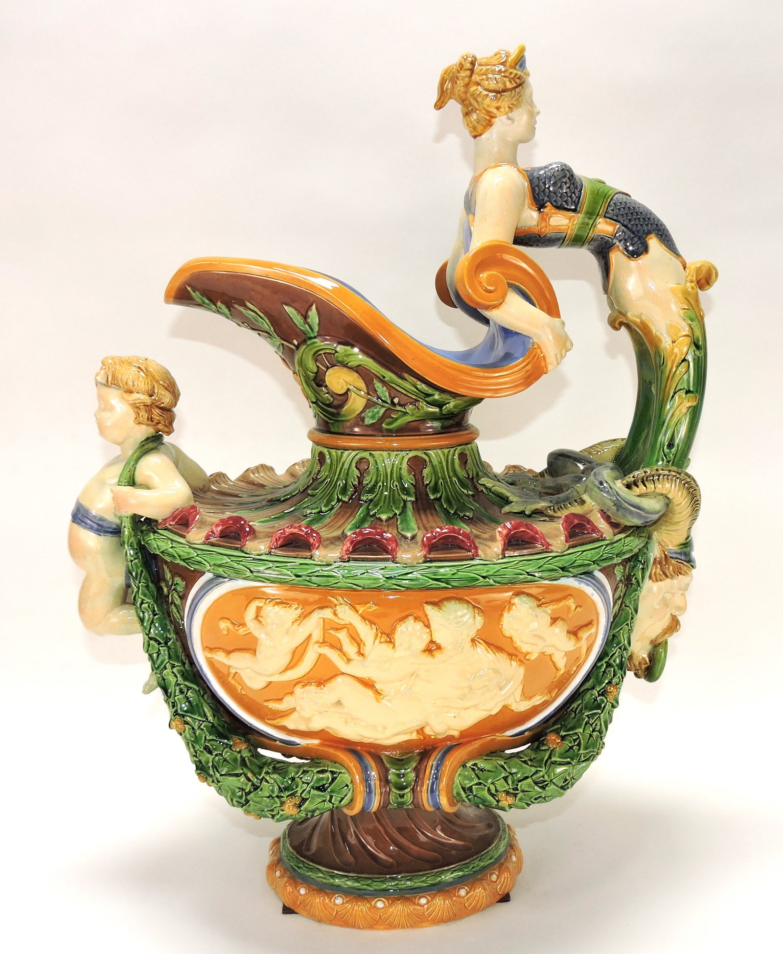 Monumental Minton majolica ewer,: 23"h, modelled with mermaid handle, her tail wrapped around a horned Bacchus mask, with laurel leaf swages running along both sides and a putto below the spout with panels in relief to either side