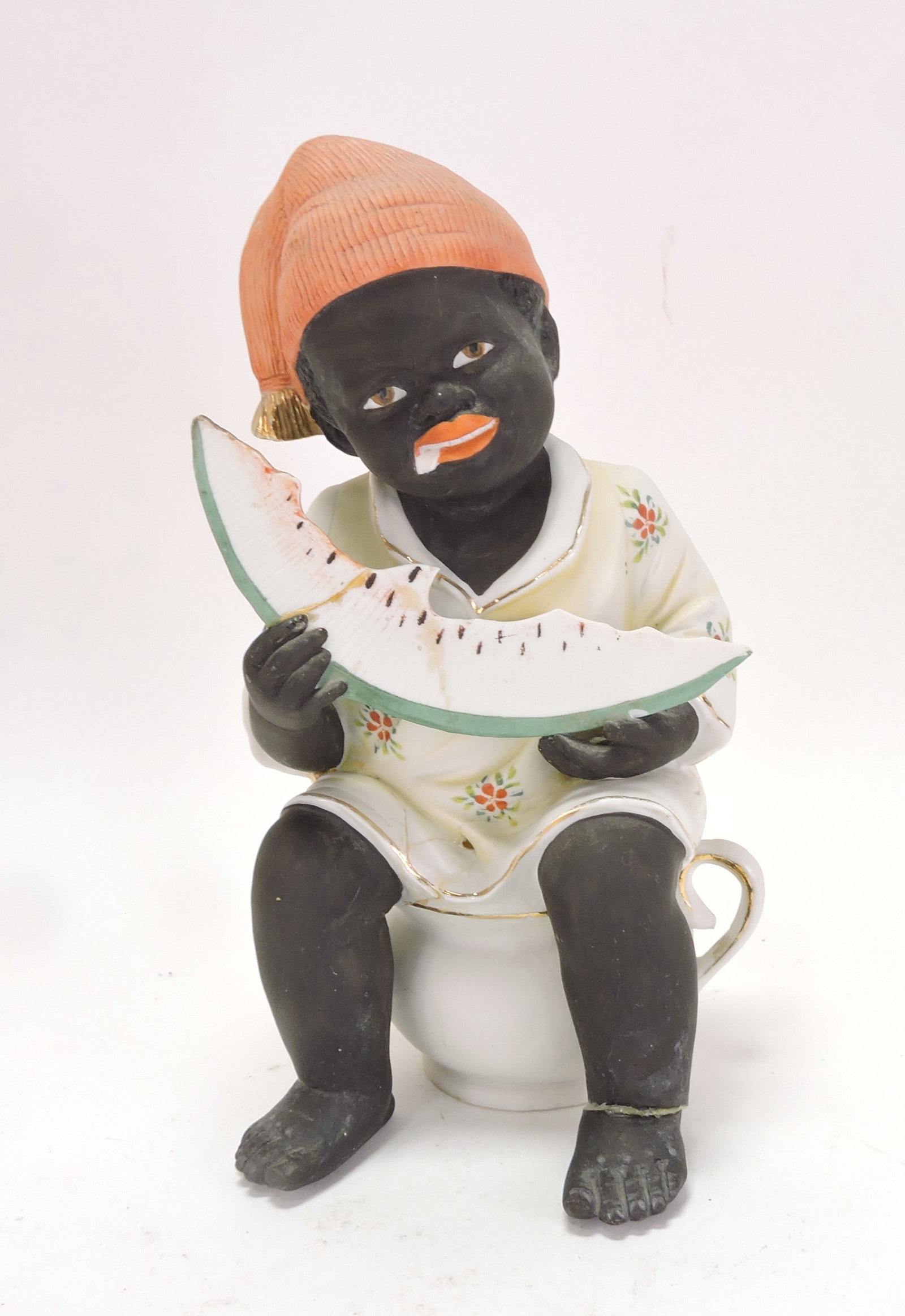Black Americana bisque figure of: boy eating watermelon seated on a cup, repair to watermelon and foot, 10"