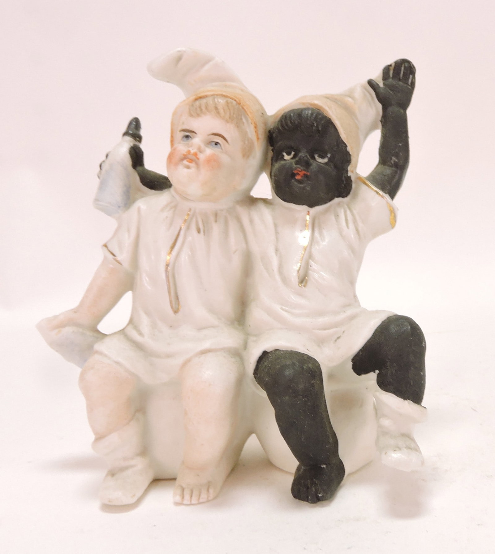 Black Americana bisque figure of: two children with milk bottle seated on tea cups, 4 1/2"