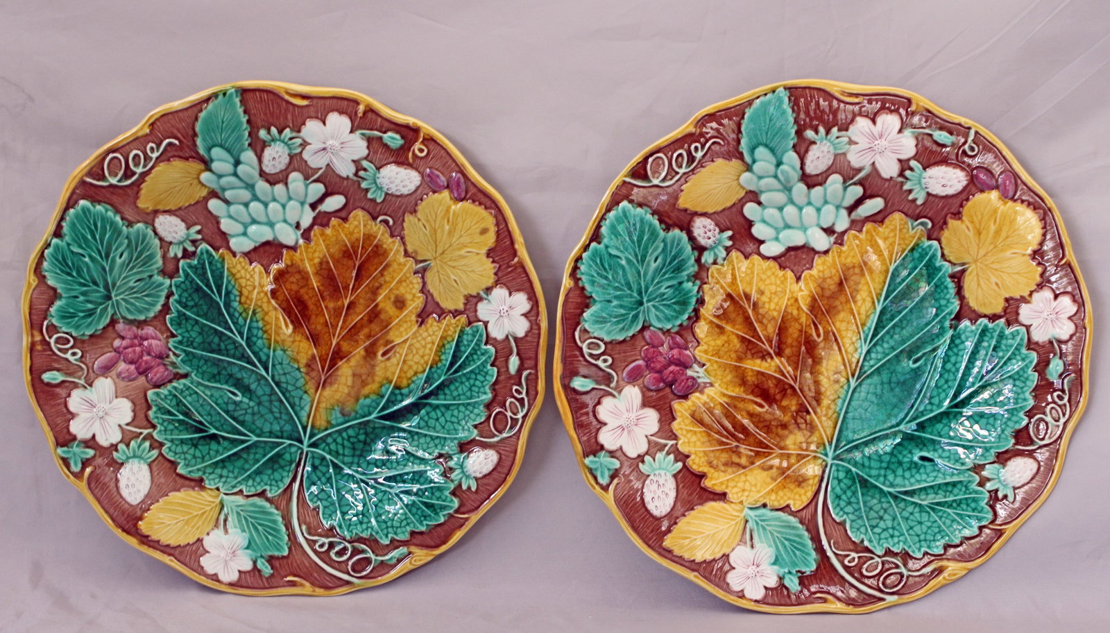 Two Wedgwood majolica strawberry plates: on a brown ground circa 1870, moulded with strawberries, grapes, leaves & flowers, yellow vine rims, impressed marks, 8 3/4 “w, date code for 1870. Ref: The Joan Stacke Graham Majolica Collectio