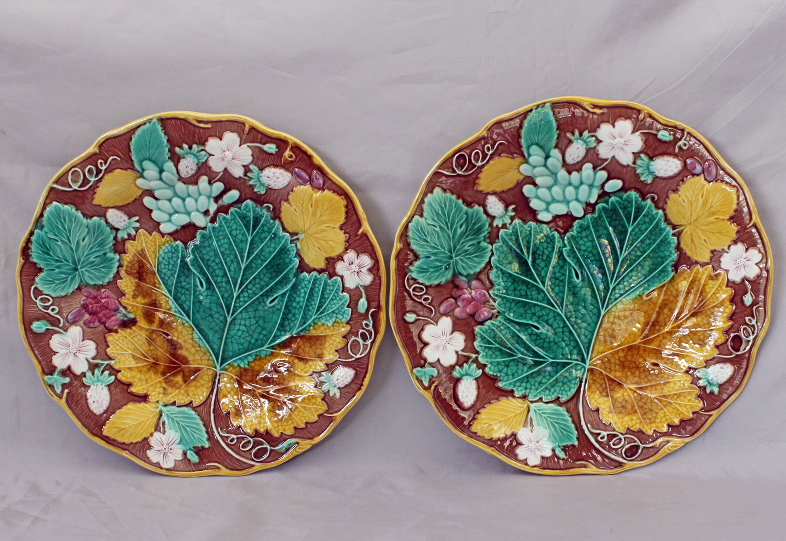 Two Wedgwood majolica strawberry plates: on a brown ground circa 1870, moulded with strawberries, grapes, leaves & flowers, yellow vine rims, impressed marks, 8 3/4 “w, date code for 1870. Ref: The Joan Stacke Graham Majolica Collectio