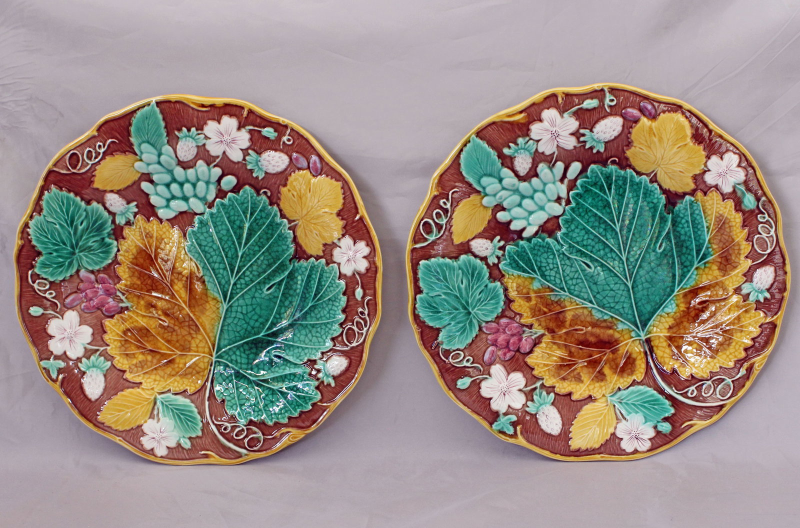 Two Wedgwood majolica strawberry plates: on a brown ground circa 1870, moulded with strawberries, grapes, leaves & flowers, yellow vine rims, impressed marks, 8 3/4 “w, date code for 1870. Ref: The Joan Stacke Graham Majolica Collectio