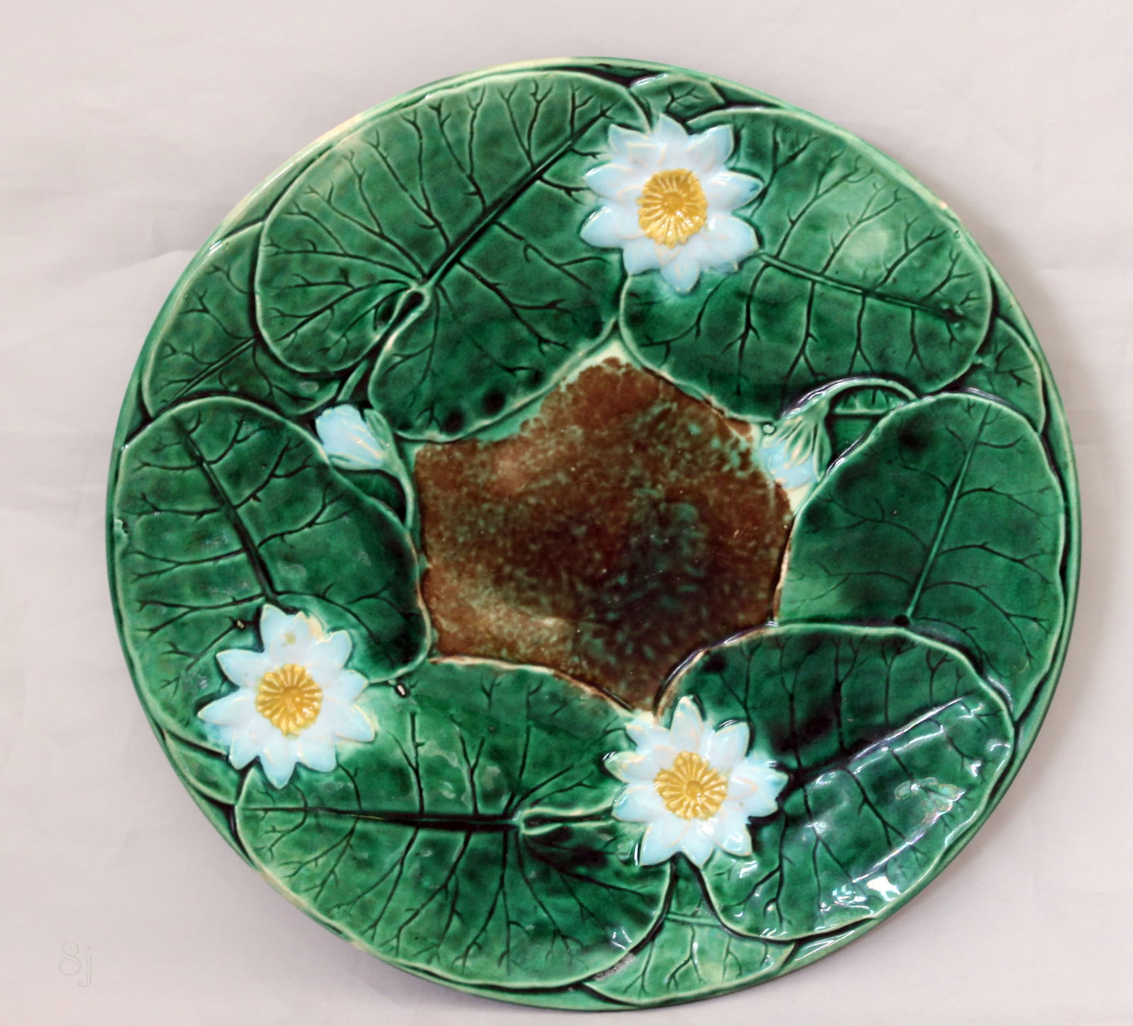 A Joeseph Holdcroft majolica plate: molded with flowering water lilies, the center formed as a pool ,makers mark to the reverse ,8 1/2"