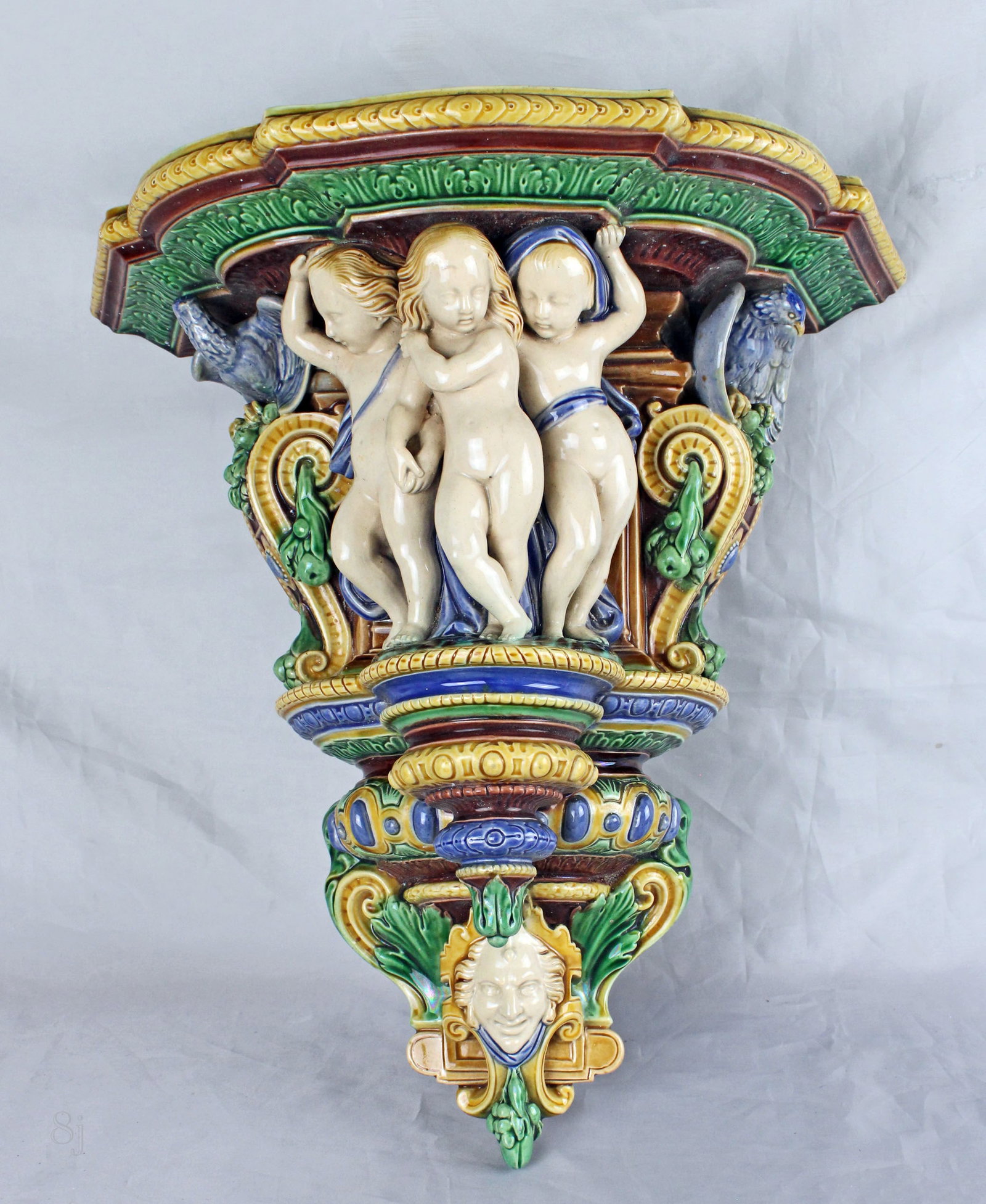 A large Minton majolica Paris wall bracket: modelled in relief with the Three Graces, below a face mask with hanging fruit & leaf detail, to either side a winged bird, impressed Minton, date code for 1863, model no. 338 to the shelf, 15"h,