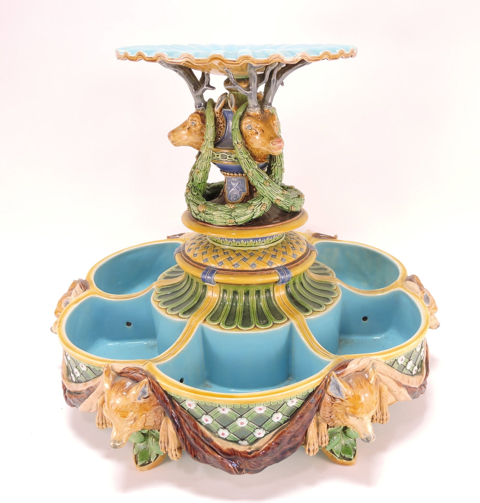 RARE Minton majolica ice stand,: shape no. 1146, designed in two tiers, the top a fluted dish supported by three stag heads draped with pine boughs and cones about a knopped stem and center section; the below tier divided into six po