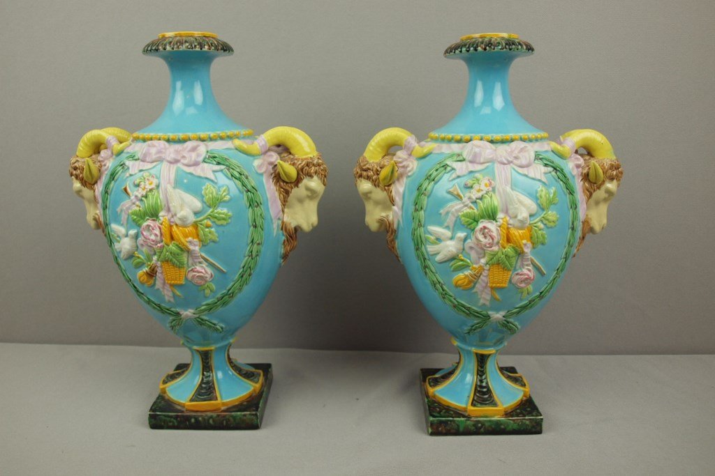 GEORGE JONES pair of majolica mantle urns with ram's: GEORGE JONES pair of majolica mantle urns with ram's head handles joined with pink ribbon and bows, one side of each decorated with basket of flowers and doves, 13 1/2", professional repair to stem of